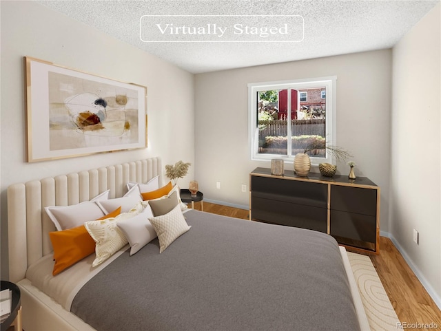 bedroom featuring baseboards, a textured ceiling, and wood finished floors