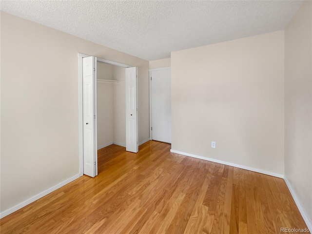 unfurnished bedroom featuring a closet, a textured ceiling, light wood-type flooring, and baseboards