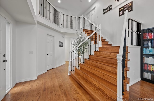 stairs with baseboards, a high ceiling, recessed lighting, and wood finished floors