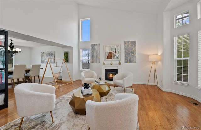 living area featuring visible vents, a glass covered fireplace, wood finished floors, baseboards, and high vaulted ceiling