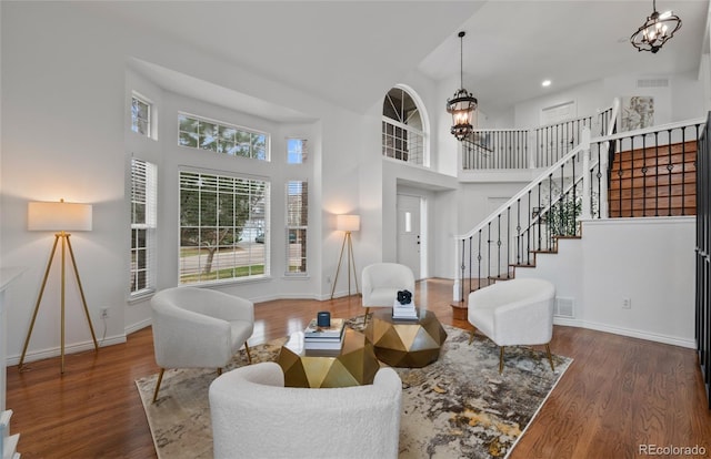 living room with stairs, a notable chandelier, wood finished floors, and a towering ceiling