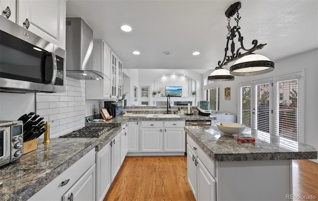 kitchen with a sink, light wood-style flooring, wall chimney exhaust hood, stainless steel appliances, and white cabinetry