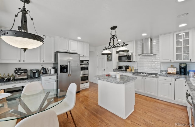 kitchen with a center island, appliances with stainless steel finishes, white cabinets, and wall chimney range hood