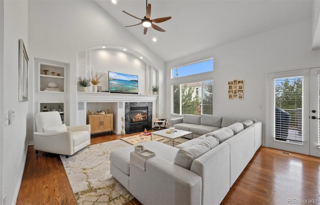living area with built in features, wood finished floors, a fireplace, ceiling fan, and high vaulted ceiling