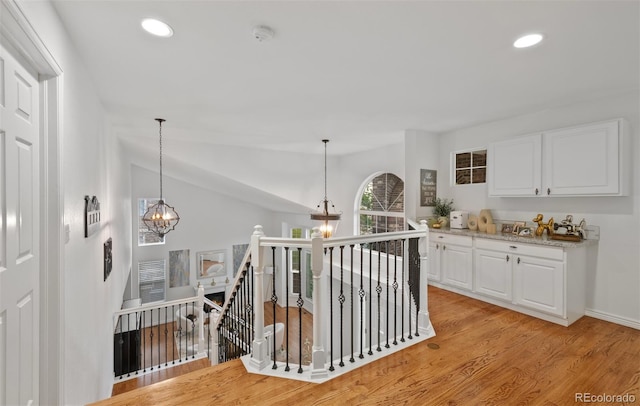 corridor with light wood-style flooring, recessed lighting, a chandelier, and an upstairs landing