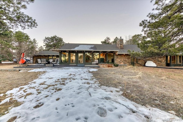 snow covered property with stone siding and a chimney