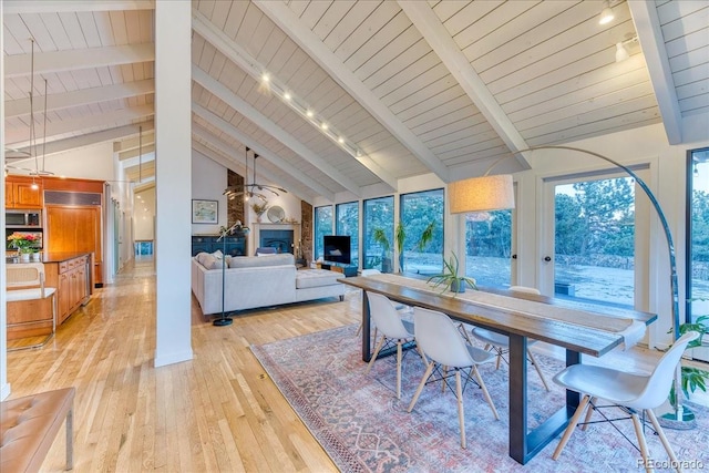 dining room featuring beam ceiling, a glass covered fireplace, wood ceiling, high vaulted ceiling, and light wood-type flooring