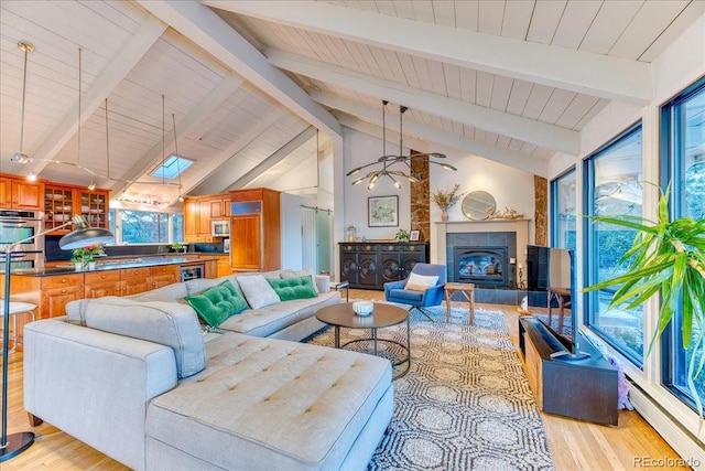 living room featuring vaulted ceiling with beams, ceiling fan, light wood-type flooring, and a tile fireplace