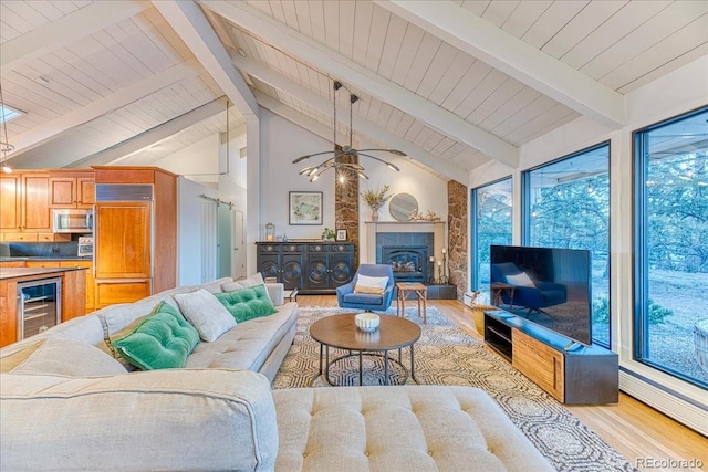 living area with a glass covered fireplace, beverage cooler, beamed ceiling, and light wood finished floors