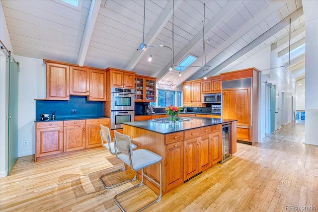 kitchen with beverage cooler, a kitchen island, appliances with stainless steel finishes, light wood finished floors, and dark countertops