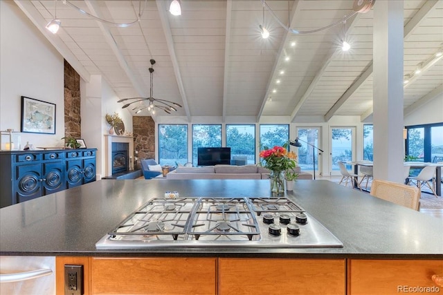 kitchen featuring a fireplace with raised hearth, dark countertops, open floor plan, vaulted ceiling with beams, and stainless steel gas stovetop