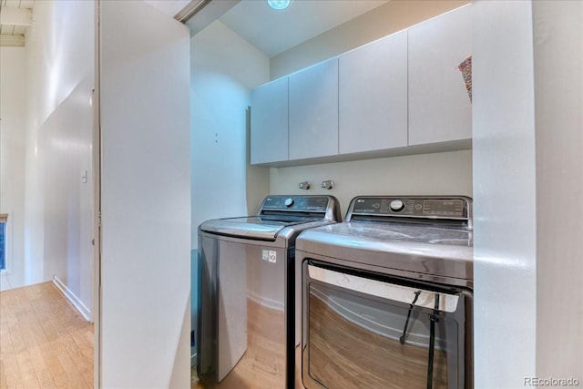 clothes washing area with light wood finished floors, washing machine and clothes dryer, and cabinet space