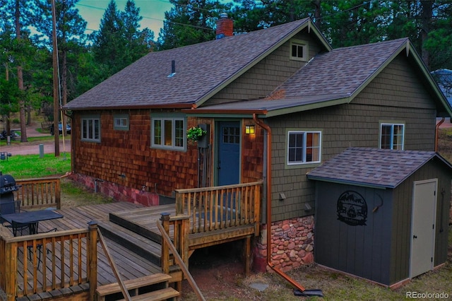 back of house with a deck, roof with shingles, and a chimney