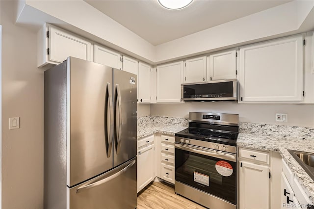 kitchen with light stone countertops, white cabinets, light wood-type flooring, and appliances with stainless steel finishes