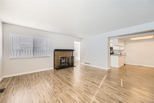 unfurnished living room with a tiled fireplace, sink, light hardwood / wood-style flooring, and a textured ceiling