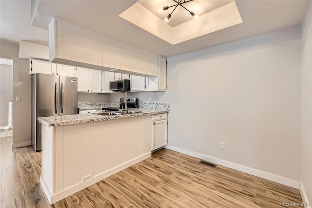 kitchen featuring appliances with stainless steel finishes, white cabinetry, kitchen peninsula, a raised ceiling, and light stone countertops