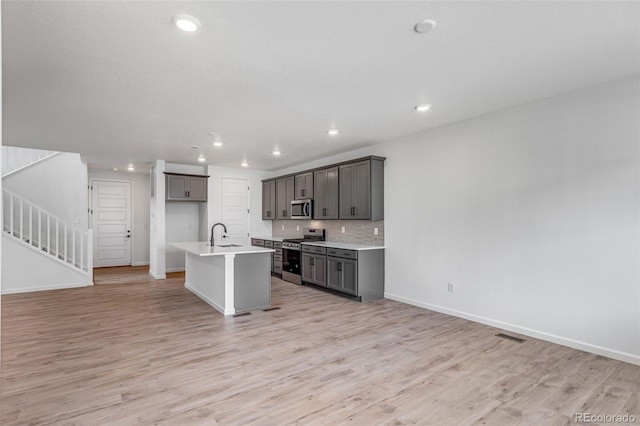 1415 Great Western Dr, Longmont, CO 80501 - kitchen featuring appliances with stainless steel finishes, light wood finished floors, a center island with sink, light countertops, and baseboards