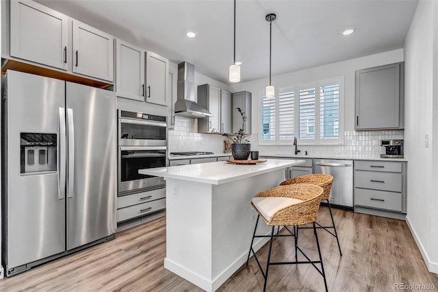 kitchen with wall chimney range hood, gray cabinetry, stainless steel appliances, a kitchen breakfast bar, and a kitchen island