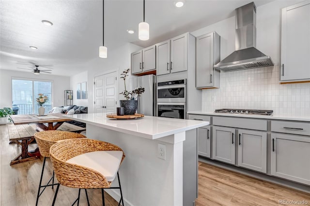 kitchen with gray cabinetry, wall chimney exhaust hood, and a kitchen bar