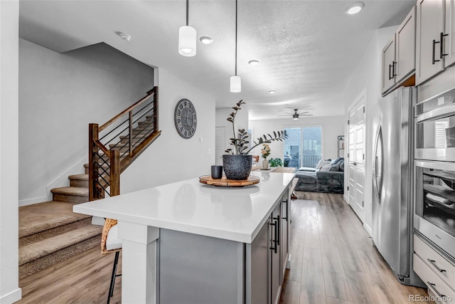 kitchen with hanging light fixtures, stainless steel fridge, a kitchen breakfast bar, and light hardwood / wood-style flooring