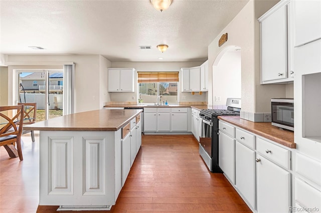 kitchen with stainless steel appliances, a kitchen island, light wood-style flooring, white cabinets, and a sink