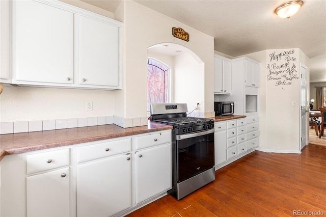 kitchen featuring appliances with stainless steel finishes, white cabinets, dark wood-type flooring, dark countertops, and arched walkways