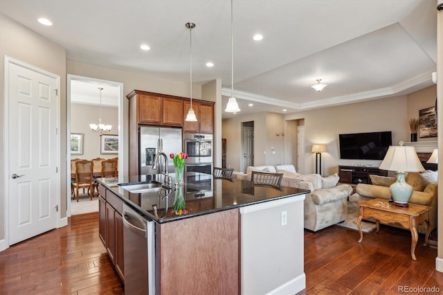 kitchen featuring a center island with sink, brown cabinetry, appliances with stainless steel finishes, decorative light fixtures, and a sink