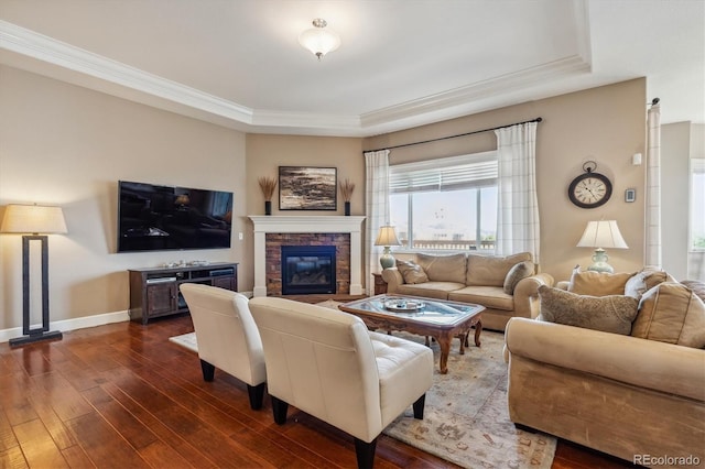 living room featuring a raised ceiling, crown molding, dark hardwood / wood-style flooring, and a stone fireplace