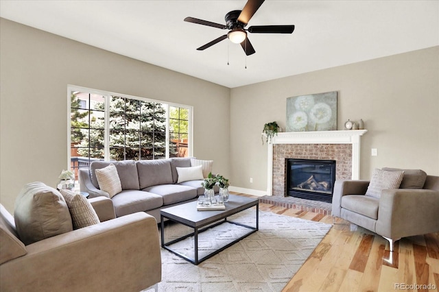 living area featuring light wood finished floors, ceiling fan, a brick fireplace, and baseboards