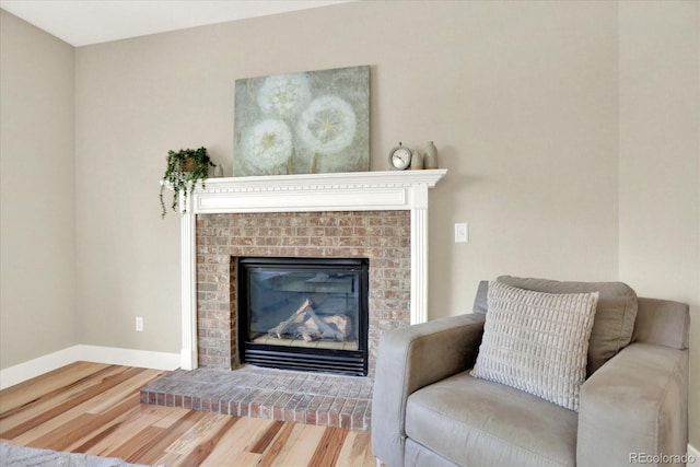 living room featuring wood finished floors, a brick fireplace, and baseboards