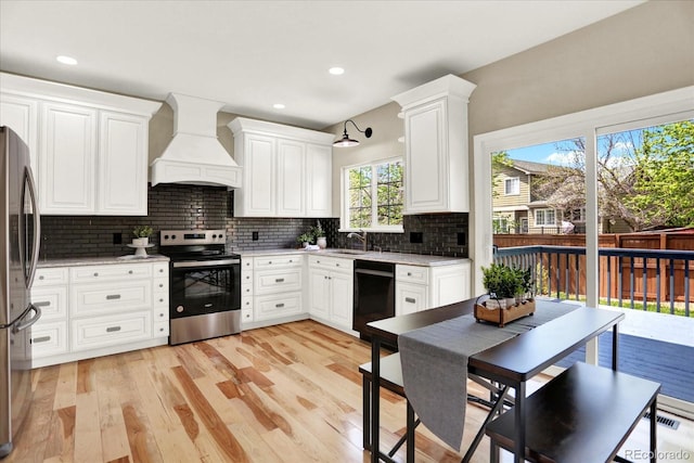 kitchen with appliances with stainless steel finishes, custom exhaust hood, a sink, backsplash, and light wood-style floors