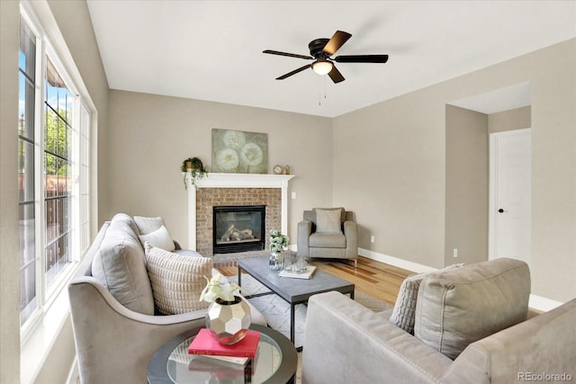 living room featuring wood finished floors, ceiling fan, baseboards, and a brick fireplace