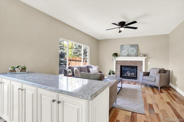 living room with light wood-style floors, a ceiling fan, a fireplace, and baseboards