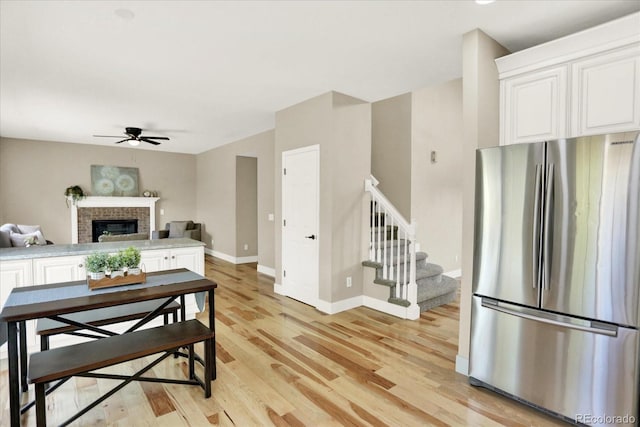 living area featuring a ceiling fan, light wood-type flooring, stairway, baseboards, and a fireplace