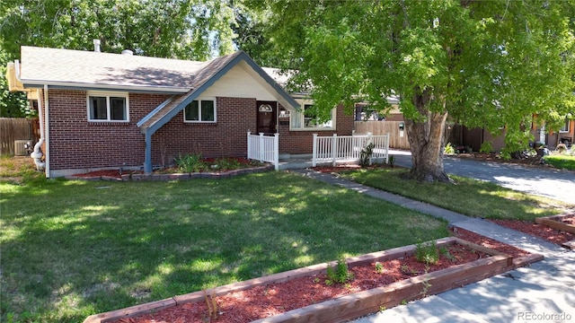 view of front of property featuring brick siding, a vegetable garden, central AC unit, fence, and a front lawn