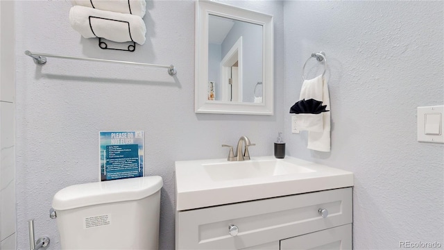 half bath with a textured wall, vanity, and toilet