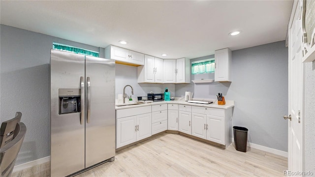 kitchen featuring stainless steel refrigerator with ice dispenser, light wood finished floors, light countertops, white cabinets, and a sink