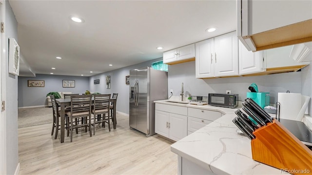 kitchen with black microwave, light stone counters, white cabinetry, stainless steel refrigerator with ice dispenser, and a sink