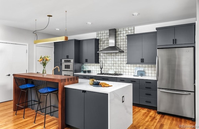 1401 Delgany St Unit 203, Denver, CO 80202 - kitchen with stainless steel appliances, wall chimney exhaust hood, a center island, backsplash, and light wood-type flooring