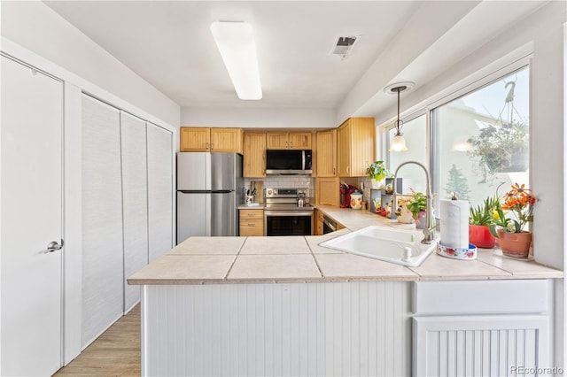 kitchen with pendant lighting, light hardwood / wood-style flooring, stainless steel appliances, kitchen peninsula, and sink