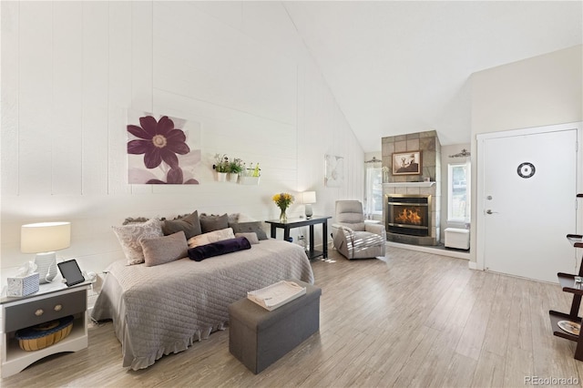 bedroom with high vaulted ceiling, a tile fireplace, and light hardwood / wood-style floors