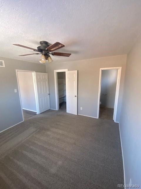 unfurnished bedroom featuring dark colored carpet, a spacious closet, a textured ceiling, a closet, and ceiling fan