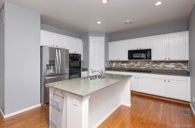 kitchen featuring black appliances, white cabinets, sink, light hardwood / wood-style flooring, and an island with sink