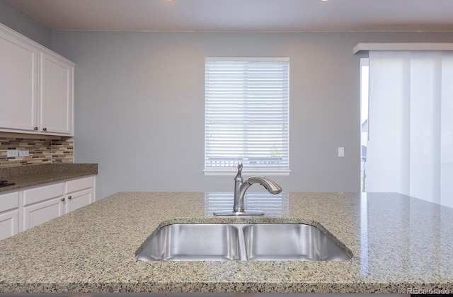 kitchen featuring light stone countertops, backsplash, a kitchen island with sink, sink, and white cabinetry