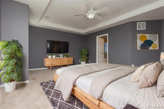 carpeted bedroom with a tray ceiling, connected bathroom, and ceiling fan