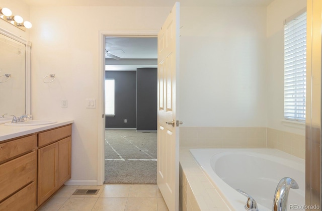 bathroom with tile patterned floors, vanity, a healthy amount of sunlight, and tiled tub