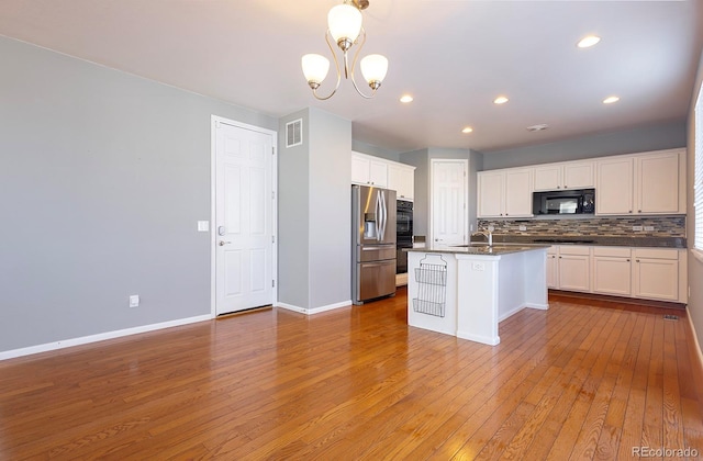 kitchen featuring appliances with stainless steel finishes, white cabinetry, light hardwood / wood-style flooring, and an island with sink