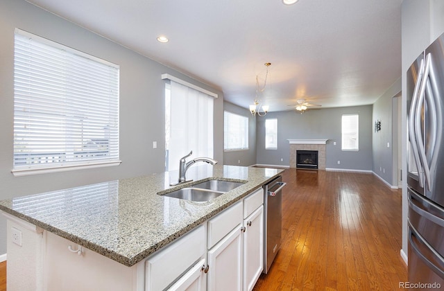 kitchen with a tile fireplace, white cabinetry, sink, hardwood / wood-style floors, and appliances with stainless steel finishes