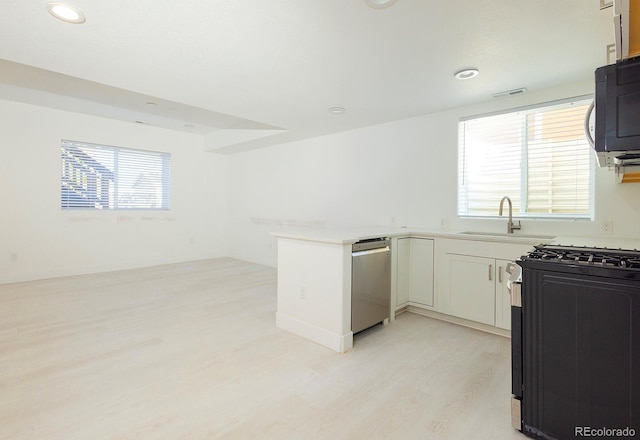 kitchen featuring sink, light hardwood / wood-style flooring, white cabinetry, kitchen peninsula, and black range with gas cooktop