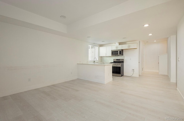 kitchen with kitchen peninsula, appliances with stainless steel finishes, decorative backsplash, white cabinets, and light hardwood / wood-style floors